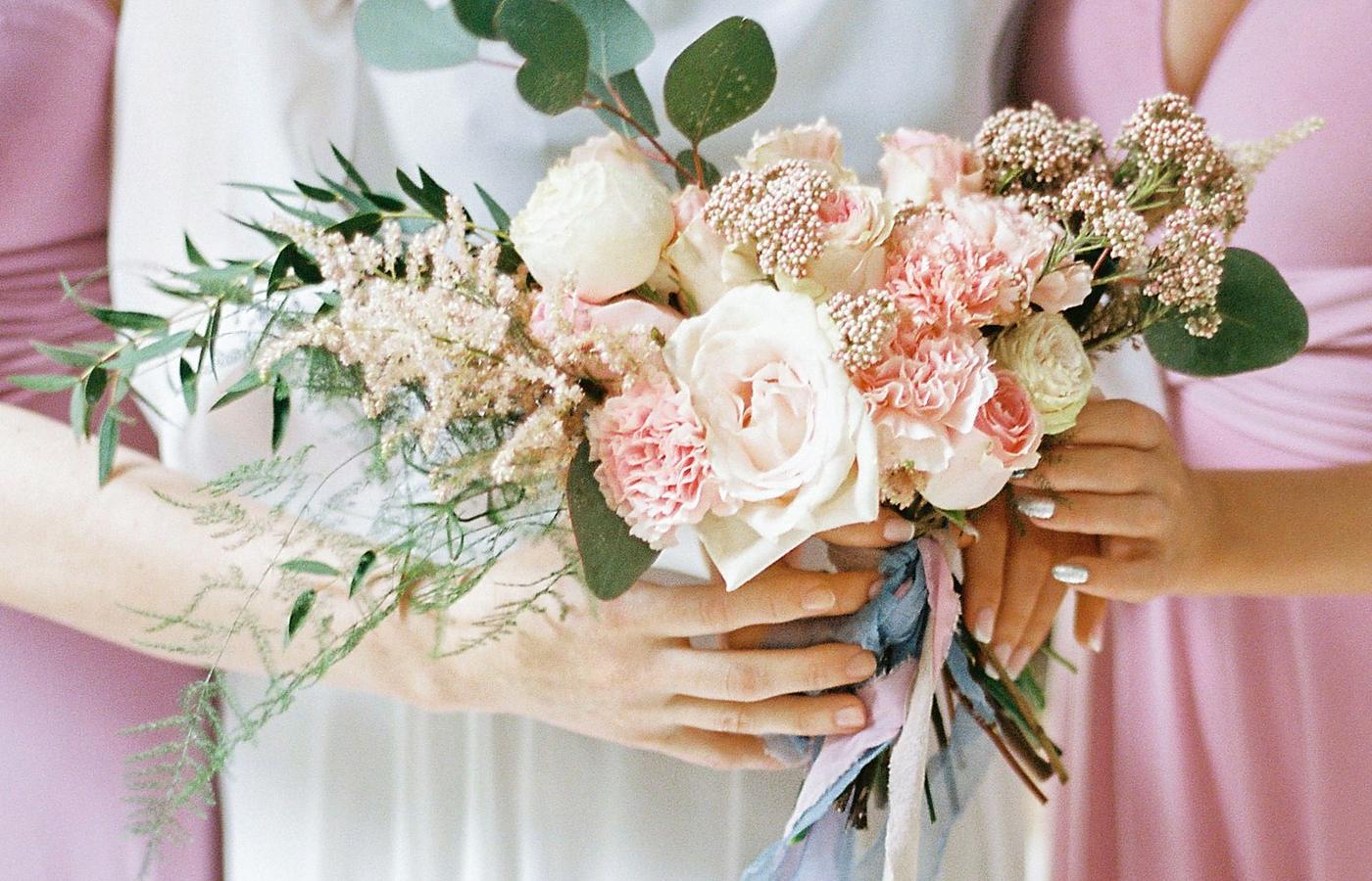 Licensed stock photograph: two bridesmaids in matching dusty rose dresses either side of an ivory gown, their hands together around a pale bouquet.