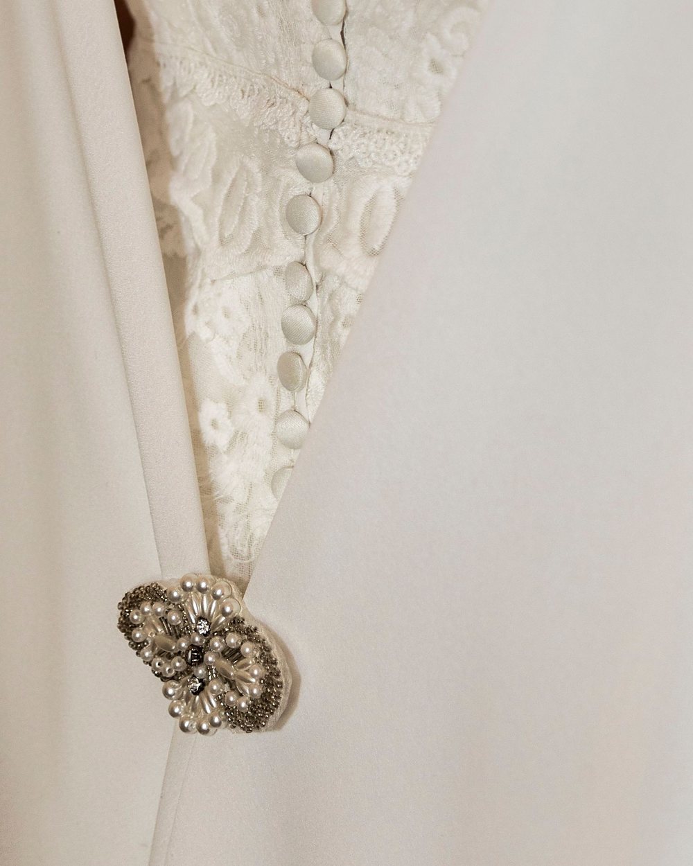 Licensed stock photograph: the ivory lace front of a dress, a row of covered buttons down the placket and a pearl brooch at the waist.