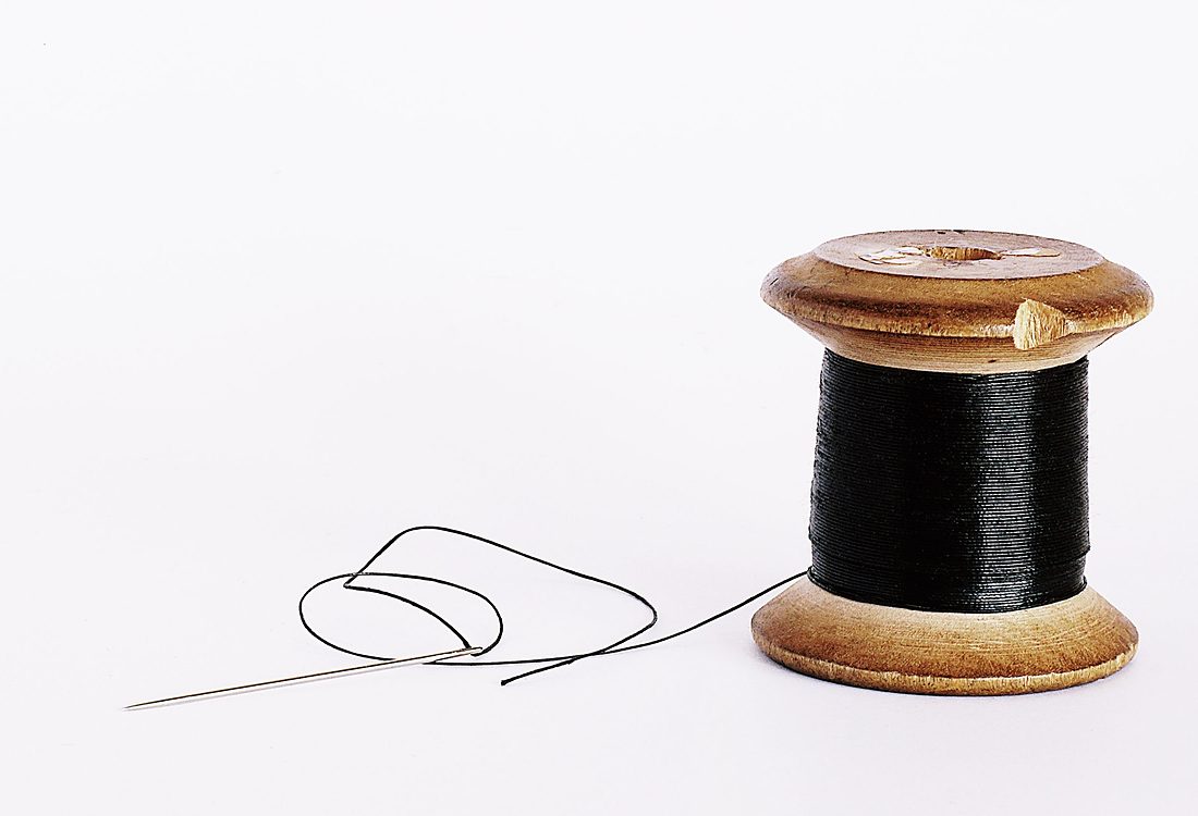 Licensed stock photograph: a wooden spool of black thread on a white surface, with a threaded needle beside it.